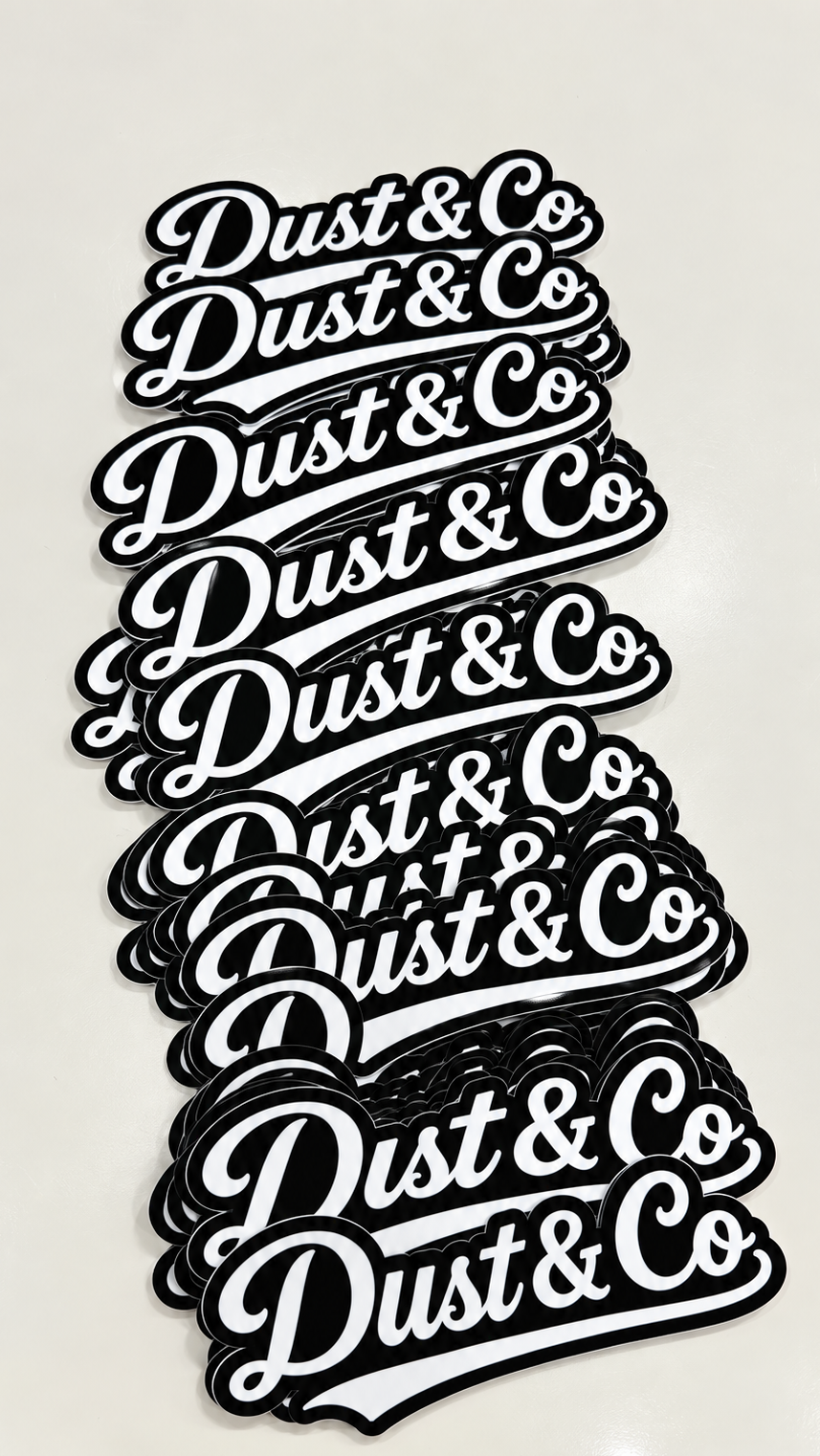A stack of black and white 'Dust & Co' logo decals or stickers, displayed on a light-colored surface.